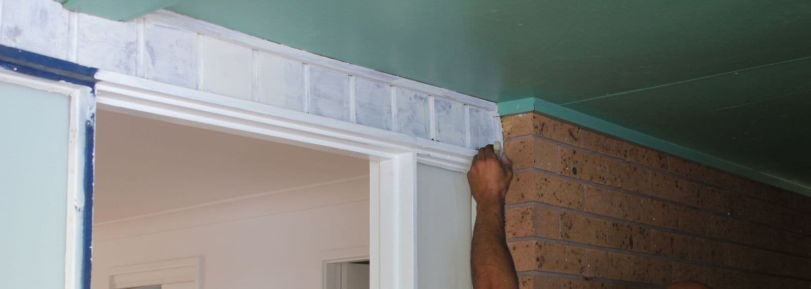 Blue masking tape along a door frame while the trim is painted by brush